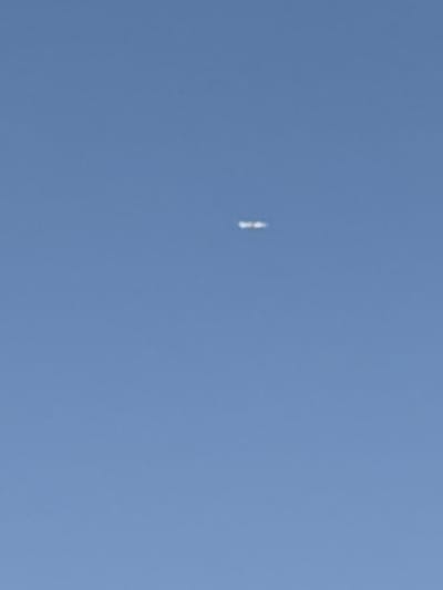 A photograph taken from a low angle shows a clear blue sky with a faint, elongated white object located in the upper central portion of the frame. The object appears to be composed of two small, distinct white dots positioned horizontally next to each other, with a slight gap in between. The overall image is out of focus, making it difficult to discern specific details about the object's shape or texture. The background is a uniform, cloudless sky, indicating an outdoor daytime setting. The image was captured in Coslada, Spain.