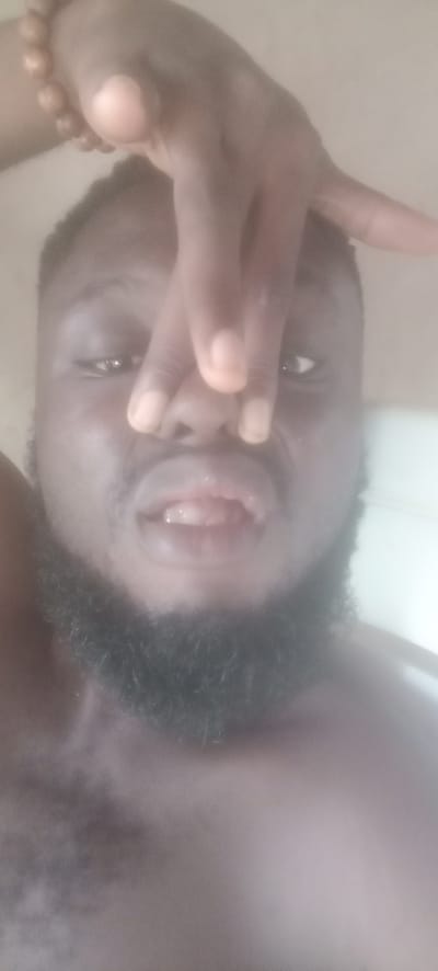 A man with dark skin and a beard is pictured from a low angle. His fingers are positioned in front of his nose, partially obscuring his face. A beaded bracelet is visible on his wrist. The image is blurry and lacks clear details of the background, making it impossible to place the location within Bende, Nigeria, or any other specific environment.