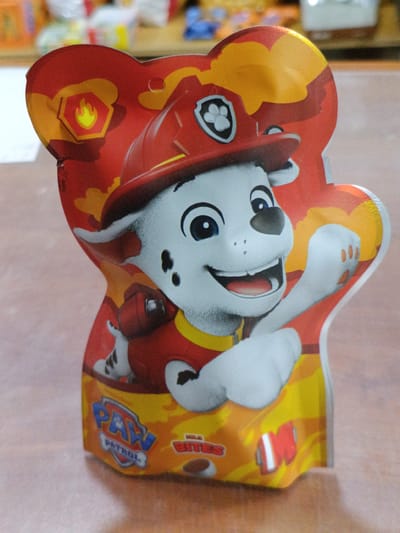 A Paw Patrol character, Marshall, is depicted on a red and orange package. The character is a white dog wearing a red firefighter's helmet and uniform. The package has a bear-like outline. The background is blurred, but appears to be a table with some indistinct items. The location is specified as Martuni, Armenia, though no specific city landmarks are visible to confirm this.