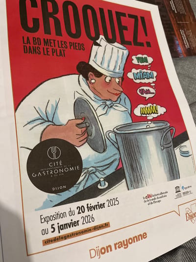 The image features a poster advertising an exhibition called "Croquez! La BD met les pieds dans le plat" at the Cité Internationale de la Gastronomie & du Vin in Dijon. The exhibition runs from February 20, 2025, to January 5, 2026. The poster depicts a chef character with thought bubbles labeled "Yumi," "Miam," "Yam...," and "Mmmm!" A website address, citedelagastronomie-dijon.fr, is also visible. Small icons of Angoulême, Dijon, and a text fragment, "la cito internationalo do la bando dossindo of do l'imago," appear in the upper right.