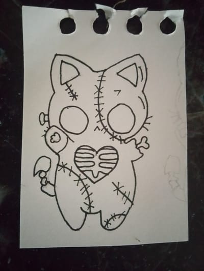 The image displays a black and white sketch on a piece of torn notebook paper. The drawing is of a Frankenstein-like cat character with stitched seams and a ribcage-shaped heart. The paper has three punched holes at the top, indicating it's from a binder. The background is dark and out of focus, suggesting it is a flat surface. There is no information in the image to suggest any location in Syasstroy, Russia.