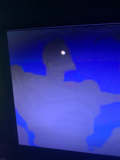 The image shows a close-up, low-resolution view of a screen displaying a dark, abstract scene dominated by shades of deep blue and white. A faint, lighter-colored humanoid silhouette is visible in the center, with a bright white light spot near its head area, possibly representing an eye or a reflection. The background is a solid, dark blue. There is no discernible urban or natural environment, and no indication of a specific location in Glodeni, Moldova, or any other city. The scene is entirely abstract and lacks any contextual details.