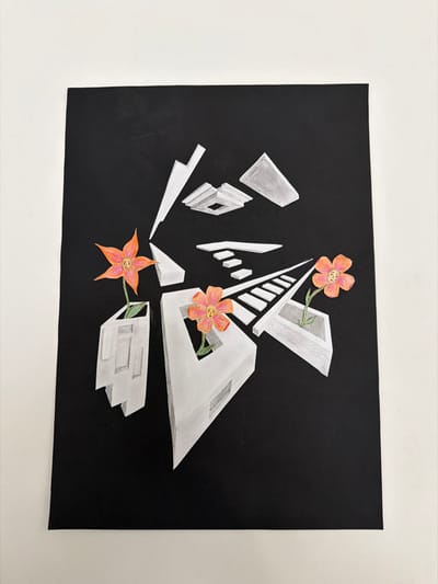 The image presents a close-up, head-on view of a vertically oriented, rectangular piece of artwork displayed against a plain, light-colored wall. The artwork features a solid black background onto which a composition of abstract, architectural-style geometric forms is rendered in white and various shades of grey. These forms create illusions of depth, featuring elements resembling stairs, platforms, and angular structures. Three stylized flowers, each with distinct orange petals, light yellow-pink centers, and small dark dots, are integrated into this geometric landscape. One flower emerges from a multi-faceted white structure on the left side of the artwork. A second flower is positioned within an open, angular white structure in the lower-right quadrant. A third flower is visible in the upper-left, also emerging from a white geometric form. Green stems are visible beneath each flower. The black surface of the artwork exhibits minor imperfections consistent with paper or card stock. The specific location in Sankt Pölten, Austria, cannot be determined from the visual content of this image.