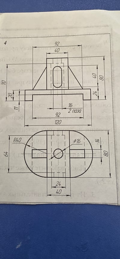 The image displays a technical drawing, likely a blueprint or engineering schematic, featuring multiple views of an object with various dimensions indicated. The drawing is printed on white paper, which appears to be slightly aged or creased in places. The background is a textured blue surface, possibly a table or a binder. There are no people, animals, or any elements related to the city of Almalyk, Uzbekistan present in the image. The drawing itself is the sole subject matter.
