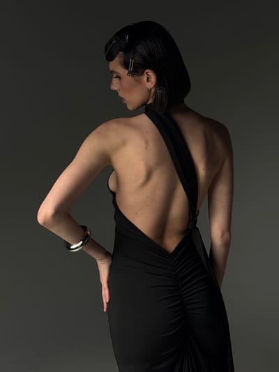 A woman with dark hair styled with two silver barrettes is photographed indoors against a grey background. She is wearing a black dress with a low-cut back and a silver bangle on her right wrist. Her head is bowed slightly, and her left hand is extended, touching the fabric of her dress. The location is likely indoors, but its relation to Northampton Township, United States of America, cannot be determined from the image alone.