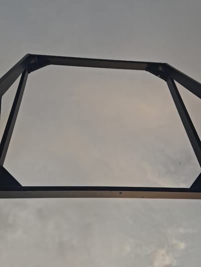 A low-angle shot depicts a rectangular metal frame structure against a cloudy sky. The frame consists of dark, possibly black, metal beams. The frame's construction includes diagonal support beams at the top and bottom corners. The sky visible through the frame is overcast with varying shades of gray. No people, specific objects, or actions are immediately discernible. The location and environment are indeterminate based on this visual information alone; the reference to Anipemza, Armenia is contextually unverified within the image itself.