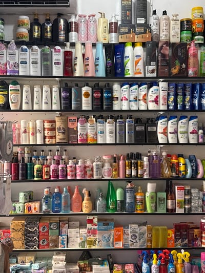 The image shows a retail shelf stacked with various beauty and personal care products, predominantly shampoos, conditioners, and body washes. The items are arranged in rows, with the majority being bottles of varying sizes and colors. Many products feature prominent branding and labels, some in English and others in what appear to be Cyrillic or Asian scripts. The lighting is bright, suggesting an indoor retail environment. The overall impression is one of a well-stocked store display. There are no people visible in the image.