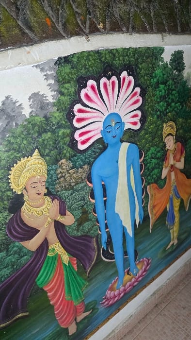 A painting depicts a reclining blue figure with a white sash, resting on a large pink and black lotus. Above, a female figure in orange and yellow robes also reclines. Below, a woman in a gold crown and purple robe raises her hands in a gesture. The background is a mix of green foliage and light blue water. The style is vibrant and evocative, reminiscent of traditional Hindu art.