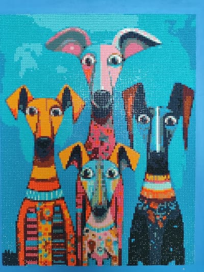 The image is a close-up, medium-shot, eye-level photograph of a diamond painting depicting five abstract, stylized dogs against a bright turquoise background. The dogs are rendered in a mosaic-like style with small, colorful beads. From left to right, the dogs appear to be of different breeds and sizes, with exaggerated features like long snouts and large ears. Each dog is wearing a vibrantly patterned sweater or collar. The diamond painting itself is framed by a solid blue border at the top and bottom. The image does not depict any recognizable elements of the city of Snezhinsk, Russia.