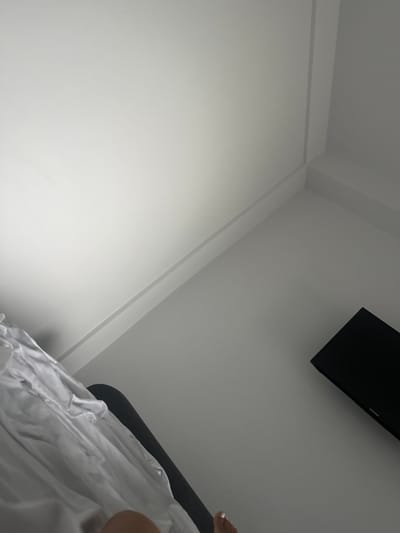 The image shows a corner of a room with white walls and a dark gray television mounted on the wall. There is also a white sheet or fabric draped over a dark object in the foreground. The lighting is dim, with a bright light source coming from the upper left corner of the image. There are no visible people in the image. The scene appears to be indoors, possibly a bedroom or living room. The location of Stațiunea Zoologică Marină Agigea, Romania, is not discernible from the visual information provided in the image.