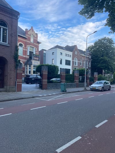 This media file shows a street scene in Weert, Netherlands. The perspective is from a low angle looking up at the sky and then down the street, with the camera rotated.
The subjects include several residential buildings of varying architectural styles, characterized by brickwork and white facades. There is a silver Volkswagen Golf parked on the right side of the street, facing away from the viewer. A black Mini Cooper is parked in the driveway of one of the houses. A green trash bin is visible on the sidewalk. Trees line the street and are visible in the background. The sky is mostly blue with scattered white clouds.
The scene appears to be during the daytime, likely late morning or early afternoon, given the lighting. The weather seems pleasant, with clear skies and daylight. The location is identifiable as a residential street in the Netherlands, indicated by the car's license plate, which is a Dutch format. There is no explicit activity or event taking place, suggesting a static street view. The overall impression is one of a quiet, everyday street in a European town.