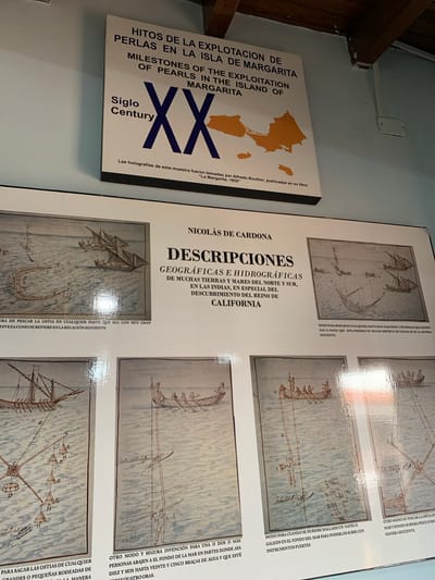 The image displays a museum exhibit featuring historical information and illustrations related to pearl exploitation on Margarita Island, Venezuela. The exhibit is mounted on a light-colored wall.

The top portion of the exhibit is a large rectangular sign with text and an orange map of Margarita Island. The title, in Spanish and English, reads "Hitos de la Explotación de Perlas en la Isla de Margarita / Milestones of Pearls in the Island of Margarita". Below this, a large graphic with "Siglo XX Century" is prominent. At the bottom of this sign, there is a caption indicating that the holographs are from the book "La Margarita" by Alfredo Boulton, published in 1952.

Below the main sign, there are multiple framed illustrations depicting historical methods of pearl fishing and exploration. These illustrations show sailing vessels, rowboats, divers, and pearling equipment in a marine environment. Each illustration has a descriptive caption in Spanish. The specific location of this exhibit in Boca del Río, Venezuela, is not provided within the visible elements of the image.