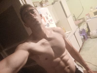 A shirtless man with a muscular physique is taking a selfie in what appears to be a kitchen. The man is positioned in the foreground, with his torso and arms prominently displayed. He is looking towards the camera with a serious expression. Behind him, kitchen cabinets and appliances are visible, along with some items on the counter and refrigerator door. The lighting is dim and appears to be artificial. There is no identifiable location of Fastiv, Ukraine, within the image.