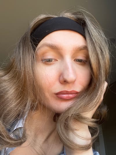 A close-up, angled portrait shows a person with fair skin and light brown hair, wearing a black headband. The person's lips are visible and appear to have been made up. The person is wearing a shirt that is partially visible. Based on the available data, the location of the image in Sepych, Russia, is unknown.