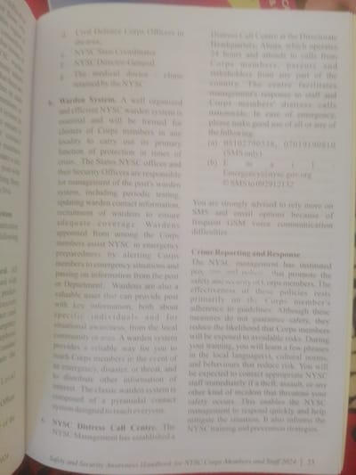 The image shows a page from a handbook with text printed in English. The text discusses "Distress Call Centre" and "Crime Reporting and Response" in the context of the NYSC (National Youth Service Corps) in Nigeria. It provides contact information for distress calls, including phone numbers and an email address: "Emergency@nysc.gov.org". The text also mentions that the NYSC management has instituted policies to promote safety and security for Corps members and staff. There is no information about the city of Magajin Gari, Nigeria, or any specific scene depicted in the image. The image is a close-up of a printed document, and no people or environmental details beyond the text are visible.