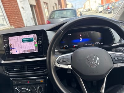 The image displays the interior of a Volkswagen vehicle, viewed from the driver's perspective, while stationary on a residential street in Preston, United Kingdom.
The dashboard features a central infotainment screen displaying a navigation map. The navigation indicates a route "Towards Maitland St," with Maitland St itself as a highlighted location. The estimated arrival time is 12:53, with 4.3 miles remaining to the destination. The current time is 12:33.
To the right, the digital instrument cluster shows a speed of 0 mph, an odometer reading of 28,217 miles, and a remaining fuel range of 160 miles. The multi-function steering wheel, bearing the Volkswagen logo and "AIRBAG" inscription, dominates the foreground. Below the infotainment screen are air vents and climate control knobs.
Through the windshield, a street scene is visible, characterized by brick terraced houses and several parked cars, under a partly cloudy sky. The vehicle is not in motion.