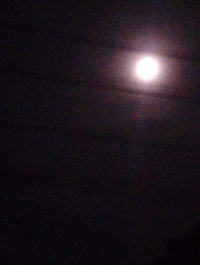 The image shows a night sky with a bright moon visible in the upper right portion of the frame. The rest of the sky is dark, with some texture visible, possibly representing clouds or other atmospheric conditions. The location, Gampongbaro, Indonesia, is not visually confirmed in the image.