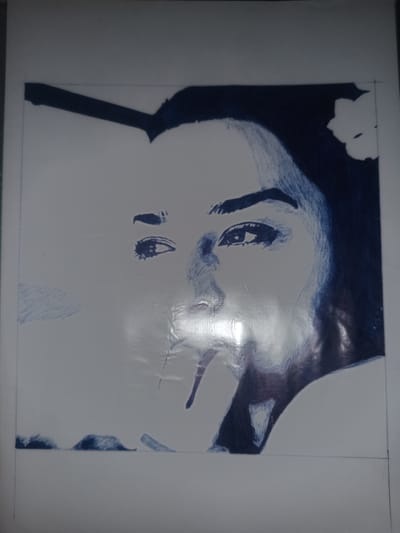 The image is a close-up of a portrait, likely a drawing or sketch, of a person's face rendered in dark blue ink on a white surface. The subject's face is partially visible, with one eye clearly defined, looking slightly to the left. The other eye is less detailed, and the nose and mouth are suggested through shading and lines. A dark mass of hair is depicted on the right side of the face, with a white flower tucked into it. The drawing appears to be in progress, with some areas more detailed than others. There are faint lines suggesting the edges of the paper or canvas, and a horizontal line dividing the upper and lower portions of the drawing. The lighting in the image causes some glare on the surface of the artwork. There is no visible text in the image. The location context provided is Gulbag, Uzbekistan, but there are no visual cues within the image to confirm this setting. The emotion conveyed is somewhat neutral, with the focus primarily on the artistic rendering of the face.