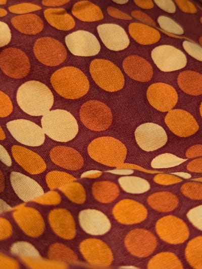 The image shows a close-up of a fabric with a polka dot pattern. The dots are of various sizes and colors, including shades of orange, yellow, and a darker burgundy. The fabric appears to be soft and possibly textured. There are no people, actions, interactions, or environmental details visible that would suggest a location in the city of Восход Снт (фролово), Russia. The image is solely a detailed view of the textile.