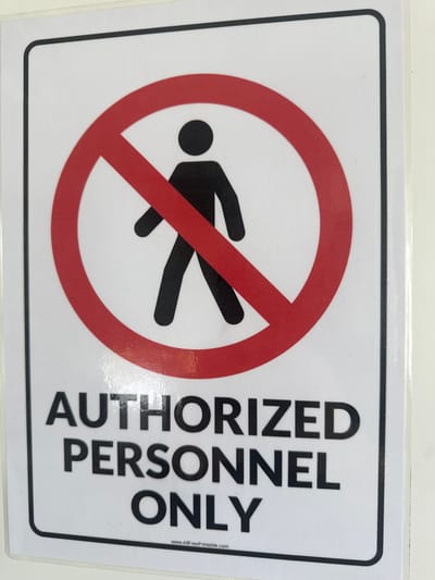 The image shows a sign with a black border on a white background. The sign has a red circle with a diagonal line through it, superimposed over a black figure of a person walking. To the right of the symbol, the words "AUTHORIZED PERSONNEL ONLY" are printed in large, black, sans-serif font, stacked vertically. The image does not provide any information that places it within the city of Diekirch, Luxembourg.