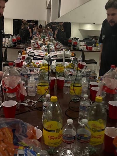 The image shows a table covered in empty bottles, red plastic cups, and food packaging. Empty Coca-Cola, Topo Chico, and Electrolit bottles are visible. Several people are reflected in a mirror behind the table, suggesting a gathering or party. The specific location in Tlalnepantla, Mexico is not discernible from the image.