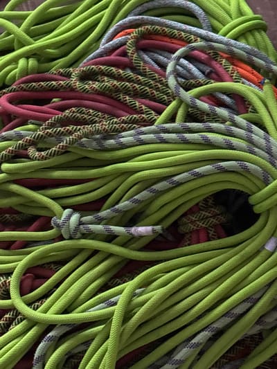 This close-up, overhead image, reportedly taken in Tayshet, Russia, depicts a dense, disordered pile of various ropes. The scene is dominated by numerous strands of vibrant lime green rope. Interspersed and intertwined with the green ropes are segments of crimson red rope, light grey ropes featuring subtle purple stripes, and ropes with a distinct black and yellow zigzag or chevron pattern. A single, simple knot is visible towards the lower-middle of the frame, tied in a light grey and green striped rope segment. The ropes are tightly packed and coiled in a seemingly haphazard manner. No individuals, actions, or specific environmental features beyond the ropes are discernible.