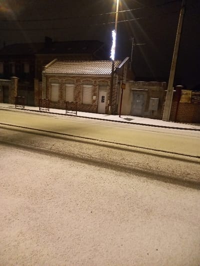 A brick building with multiple stories stands next to a bright street. The windows are covered. A street light illuminates the scene. Power lines are visible above the building. The foreground shows a sidewalk. The image is rotated counter-clockwise.
