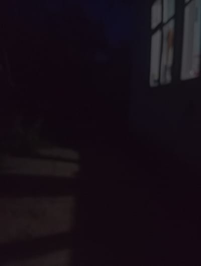 The image shows a dimly lit scene, with the majority of the frame appearing dark. In the upper left portion of the image, there are several rectangular shapes that appear to be lights, possibly ceiling lights or lights from a window. These lights are horizontal and have a slightly blurry appearance. Below these lights, there are more rectangular shapes, some of which have a reddish-brown hue. These could also be part of a window or a structure.
In the lower right portion of the image, there are vertical, abstract shapes of light and shadow. These are indistinct and appear to be reflections or silhouettes of objects or a scene outside the frame. The overall impression is of a dark interior space with some light sources or reflections. There is no clear indication of people or specific activities. The scene appears to be indoors, given the presence of what looks like artificial lighting. The location context of Зертас ауылдық округі, Kazakhstan, does not provide any direct visual cues within the image itself. No text is visible in the image.