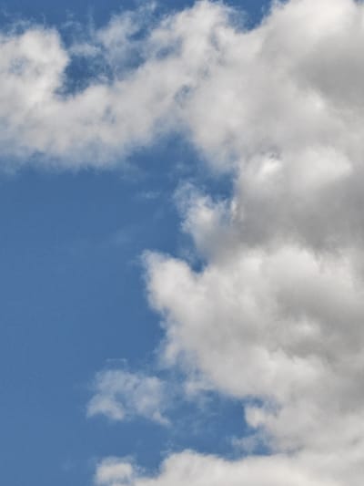 The image shows a close-up view of a blue sky with fluffy white and gray clouds. The clouds are dense and appear to be in motion, with some areas lighter and others darker, suggesting varying depths and light exposure. The sky is clear and bright, with no visible landforms or structures. The location in the city of Zyuzino, Russia, is not discernible from the image itself, as it solely depicts the sky. There are no people, objects, or actions visible. The environment is atmospheric, characterized by the natural formation of clouds against a clear sky.