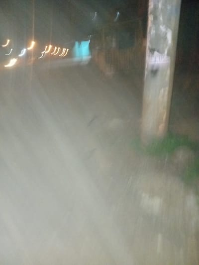 A blurred image appears to show a road or surface at night, possibly viewed from a moving vehicle. There's a horizontal beam or structure with some visible markings above. Below, streaks of light suggest streetlights or headlights. The overall impression is one of motion and low visibility. The color palette is muted, dominated by grays and whites, with faint hints of green and blue.