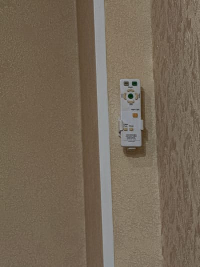 A white remote control is mounted on a textured beige wall, vertically aligned. The remote has several buttons labeled "OFF," "Bright," "Cool," "Dim," and "Warm." Below these, there are buttons for "Night Light," "Glare Free," and "Sleep." The bottom of the remote features the logo "SUPER NOVA." The wall has a subtle patterned texture, and a thin white vertical trim piece is visible to the left of the remote. The background wall to the right of the remote has a more pronounced, swirling pattern. The location is the city of Borissoglebskoye, Russia.