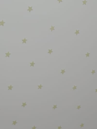 The image shows a close-up view of a pale, textured surface, possibly wallpaper, with a repeating pattern of small, yellow, five-pointed stars. The stars are evenly distributed across the surface, creating a whimsical and celestial theme. There are no people or other objects visible in the image, and the background is a uniform light color. The scene is static and appears to be an indoor setting, likely a wall. The image does not provide any information about the city of Syzran, Russia.