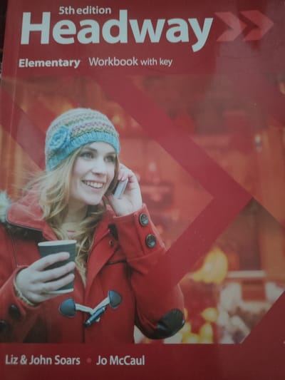 This is an image of the cover of a book titled "Headway: Elementary Workbook with Key, 5th edition." The cover features a close-up of a smiling young woman wearing a red coat and a blue knitted hat. She is holding a dark cup in her left hand and talking on a silver mobile phone to her right. The background is a blurred red abstract design with diagonal lines. The bottom of the cover displays the names "Liz & John Soars" and "Jo McCaul." There is no indication of the book's location being in Kyngyr, Uzbekistan.