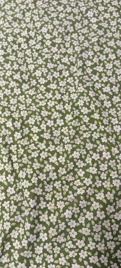 The image shows a close-up of a green fabric with a repeating pattern of small white flowers and light green leaves. The flowers have five petals and a green center, and they are scattered across the fabric in a dense, uniform arrangement. The leaves are small and ovate, also appearing in a scattered pattern around the flowers. The fabric appears to be a soft textile, possibly cotton or a blend, with a slightly textured surface. There are no people or any specific environmental elements visible that would indicate a location in Хацежынскі сельскі Савет, Belarus. The focus is entirely on the textile pattern.