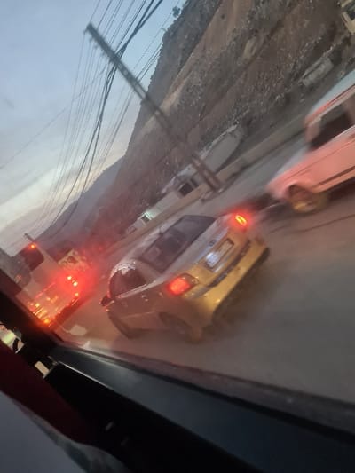 An oblique view captures a street scene with vehicles. A gold car with illuminated brake lights occupies the central part of the frame. Above it, a white vehicle is partially visible. In the lower portion, emergency lights suggest a fire truck or similar vehicle. Power lines crisscross the sky in the background, and a hillside is noticeable behind the road. The perspective is skewed, potentially taken from an elevated position.