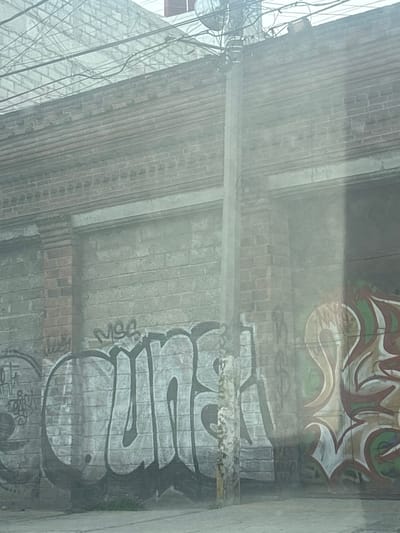 A low-angle, blurry shot of an outdoor scene in what appears to be Buenavista, Mexico. A brick underpass is covered in graffiti, featuring tags and larger art pieces. Power lines crisscross the top left of the frame.