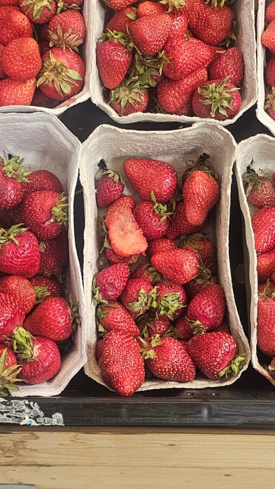 The image shows several containers of strawberries, likely on display for sale. The strawberries are bright red and appear fresh. The containers are made of a light-colored, possibly cardboard, material. The scene is likely a market or store in Rüsselsheim am Main, Germany, although specific architectural details are not visible. The overall impression is one of abundance and freshness.