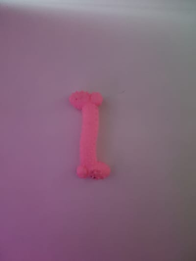 A pink, phallic-shaped object is centrally placed on a pale, textured surface. The object has a textured surface, with small raised bumps, and appears to be made of a soft material like dough or clay. The lighting in the image is dim, with a gradient of light from purple on the left to grey on the right. The background is plain and shows no discernible features. The location in the city of Гапкин, Russia is not discernible from the image.
