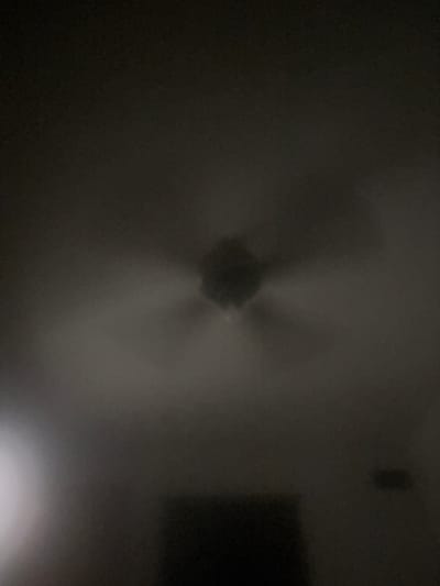 The image, taken in Kaiser, United States, is a dark, blurry photograph of a ceiling fan. The fan is the central subject, appearing as a dark, indistinct shape with visible blades. The surrounding area is also dark, with some lighter areas that could indicate ambient light sources or reflections. The overall impression is one of low light conditions, making it difficult to discern specific details about the room or its contents.