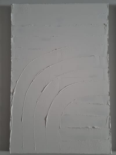 This is a close-up, horizontal, eye-level shot of a textured, monochrome artwork. The artwork is predominantly gray, with subtle variations in shade suggesting a thick impasto painting or a stuccoed surface. The texture is the main subject, characterized by distinct, parallel ridges of material applied in vertical strokes on the left side of the frame, and in sweeping, curved strokes on the right. These curved strokes create a sense of depth and movement, resembling a fanned-out pattern or a series of waves. The edges of the material are rough and uneven, adding to the tactile quality of the surface. There are no discernible figures, objects, or environmental elements; the focus is entirely on the abstract textural qualities of the artwork itself. The lighting appears to be even, casting minimal shadows and highlighting the three-dimensional surface of the material. There is no visible text or indication of a specific time of day, weather, or emotion, beyond the inherent textural interest of the piece. The setting is implied to be an indoor space where art is displayed, given the nature of the subject.