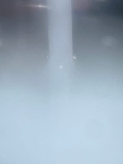 The image depicts a close-up of a textured, light blue surface, possibly a wall or fabric. There are subtle variations in shading, with some areas appearing slightly darker or more greyish. Two small, bright specks of light are visible on the surface, one slightly above and to the left of the other. To the left of the frame, a vertical streak of light with a slightly golden hue is present, suggesting a light source or reflection from the side. The overall impression is abstract and minimalist, with no discernible objects, people, or specific setting. The lighting is soft and diffused, and the image lacks any clear indicators of time of day, weather, or location, apart from the provided context of Letterkenny, Ireland. There is no visible text in the image.