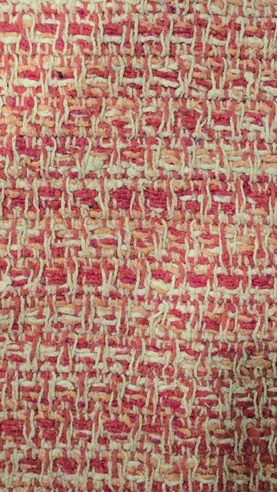The image showcases a close-up view of a woven fabric. The texture is intricate, revealing a dense grid-like pattern of interwoven threads. Predominantly, the colors are a blend of pale yellow and muted red. The weave has a slightly rough and uneven appearance, with the red and yellow threads creating a visually dynamic effect. The density and the arrangement of the threads make a textural composition.
