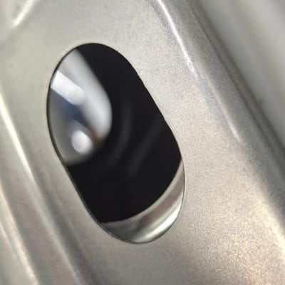 The image is a close-up, macro shot of a metal object with a textured surface and an oval-shaped opening. The metal appears to be brushed aluminum or a similar material, with visible grain and subtle variations in sheen due to the lighting. The oval opening reveals a dark, indistinct interior, possibly a cavity or a shadowed space. The foreground is dominated by the textured metal, with a strong diagonal line formed by a raised ridge or curve on the surface. The lighting creates highlights and shadows that emphasize the contours and texture of the metal. The context of Rastatt, Germany, is not visually represented in the image.