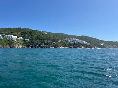 A picturesque scene displays a tranquil body of water against a verdant hillside dotted with white buildings. The hillside, covered in lush green trees, rises gently from the water's edge. The blue sky provides a serene backdrop. The composition evokes a sense of calm and relaxation.