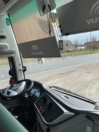 The image shows the interior of a Yutong bus, likely in transit, based on the view of a road and buildings outside the windshield. The dashboard, steering wheel, and various controls are visible, as well as a Yutong-branded sunshade. The road appears to be a rural or suburban thoroughfare, based on the presence of houses and utility poles. While the precise location in Bol'shoe Teshkovo cannot be definitively determined from the image alone, the buildings and general scenery outside the window align with typical landscape features in the area. No people are visible in the image.