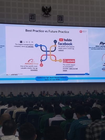 The image shows a presentation slide projected onto a large screen in an auditorium. The slide's title is "Best Practice vs Future Practice". It features logos and descriptions of several companies, including Uber, Facebook, Alibaba Group, and Airbnb, highlighting their business models. The auditorium is filled with an audience seated in rows of chairs, many of whom are wearing green shirts. At the front of the auditorium, a group of people are seated at a long table behind a green tablecloth, with some individuals appearing to be presenters or officials. A banner at the bottom of the screen indicates the event is taking place in the "Auditorium Tgk. Abdul Wahab Dahla Wy, Senin, 22 Juni 2026". The presence of the title "Auditorium Tgk. Abdul Wahab Dahla Wy" suggests the location is in Reuleut Timu, Indonesia, as this is a known landmark in that area. The overall scene depicts an academic or professional conference or seminar.