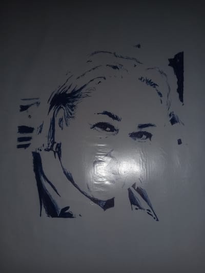 A pen sketch of a person's face is drawn on a white surface. The sketch is in dark blue ink and is incomplete, with some areas more detailed than others. The face appears to be looking forward, with the eyes being the most detailed feature. The hair is depicted with quick, energetic lines. The background is a solid white surface with a subtle texture, possibly a wall or a large sheet of paper. There is a faint reflection on the right side of the image, indicating a light source. The overall impression is of an unfinished artistic rendering. The location is stated to be Gulbag, Uzbekistan, but there are no discernible elements in the image that specifically indicate this location.