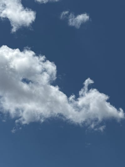 The image displays a clear blue sky with several white cumulus clouds. The clouds are scattered across the frame, with larger formations in the lower and upper left, and a more wispy formation in the upper right. There are no visible signs of human activity, buildings, or any specific landmarks that would indicate a location within the city of Nova Odesa, Ukraine. The scene is solely focused on the atmospheric conditions of the sky.