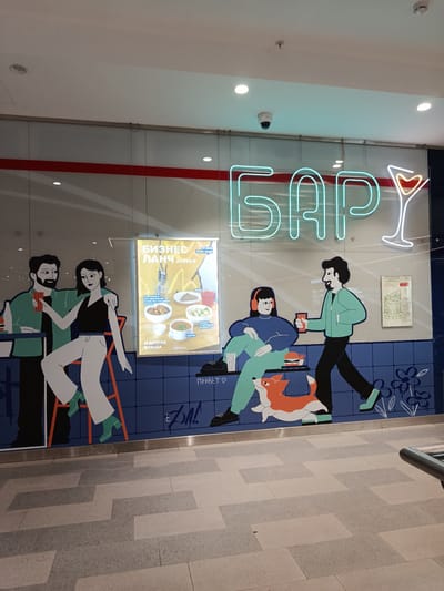 The image depicts a storefront mural in Trekhgorka, Russia. The mural features stylized cartoon figures of people in a casual bar setting. The figures include a man and woman at a counter, a person sitting with a dog, and another man walking with a drink. A neon sign spelling "БАР" (BAR) in Russian is above the mural. A menu for "БИЗНЕС ЛАНЧ" (BUSINESS LUNCH) is displayed, offering dishes and prices. A floor plan of the location is also visible. The scene takes place in a shopping mall. The floor is tiled with a geometric pattern.