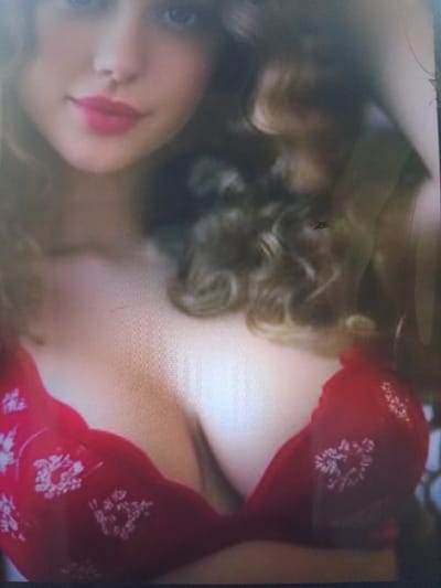 The image is a close-up, slightly blurry photograph of a woman. She has fair skin and is wearing a red bra with a floral pattern. Her lips are painted pink. Her hair is curly and brown. The background is out of focus and appears to be an indoor setting. There is no discernible information about the city of Dobra Krynytsia, Ukraine, or any specific environmental details.